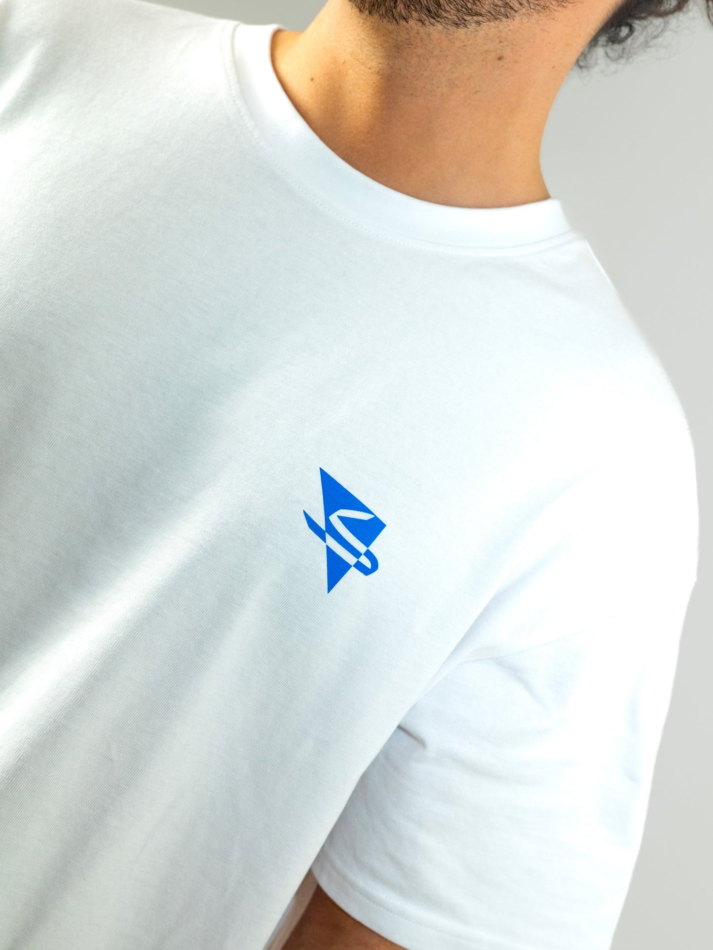 Close up of a beautiful arab model wearing a cool and creative over-sized t-shirt for streetwear and everyday lifestyle clothing. It features a simple beautiful logo, which is geometric in design and that has an arabic letter within it. White t-shirt. Frontside view. Blue print color.