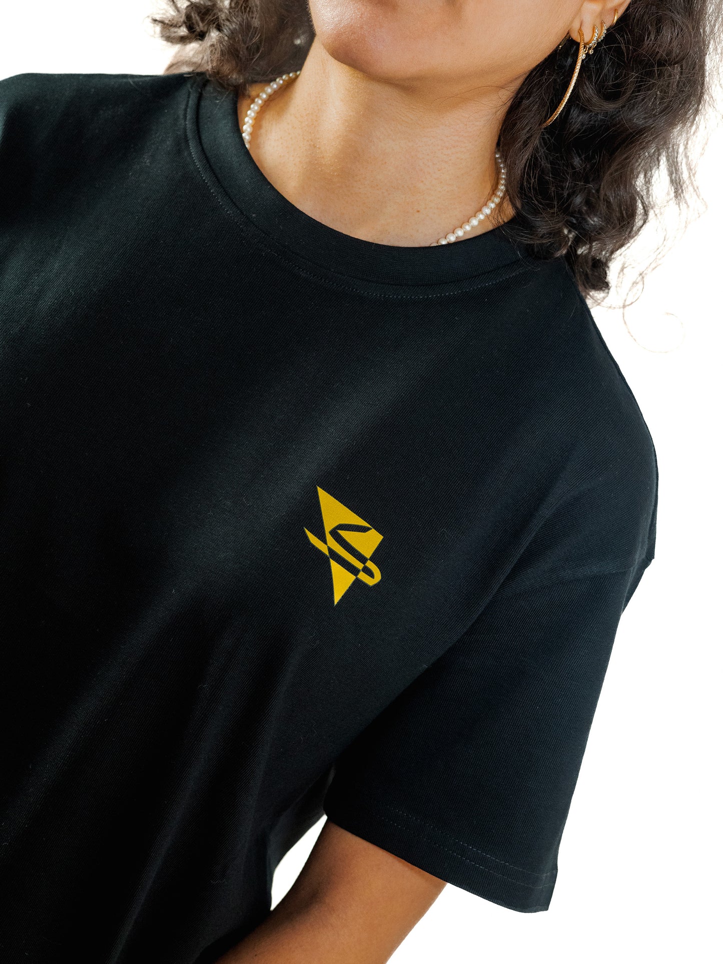Close-up of a beautiful arab model wearing a cool and creative over-sized t-shirt for streetwear and everyday lifestyle clothing. It features a simple beautiful logo, which is geometric in design and that has an arabic letter within it.  Black t-shirt. Frontside view. Black and yellow, gold print color.