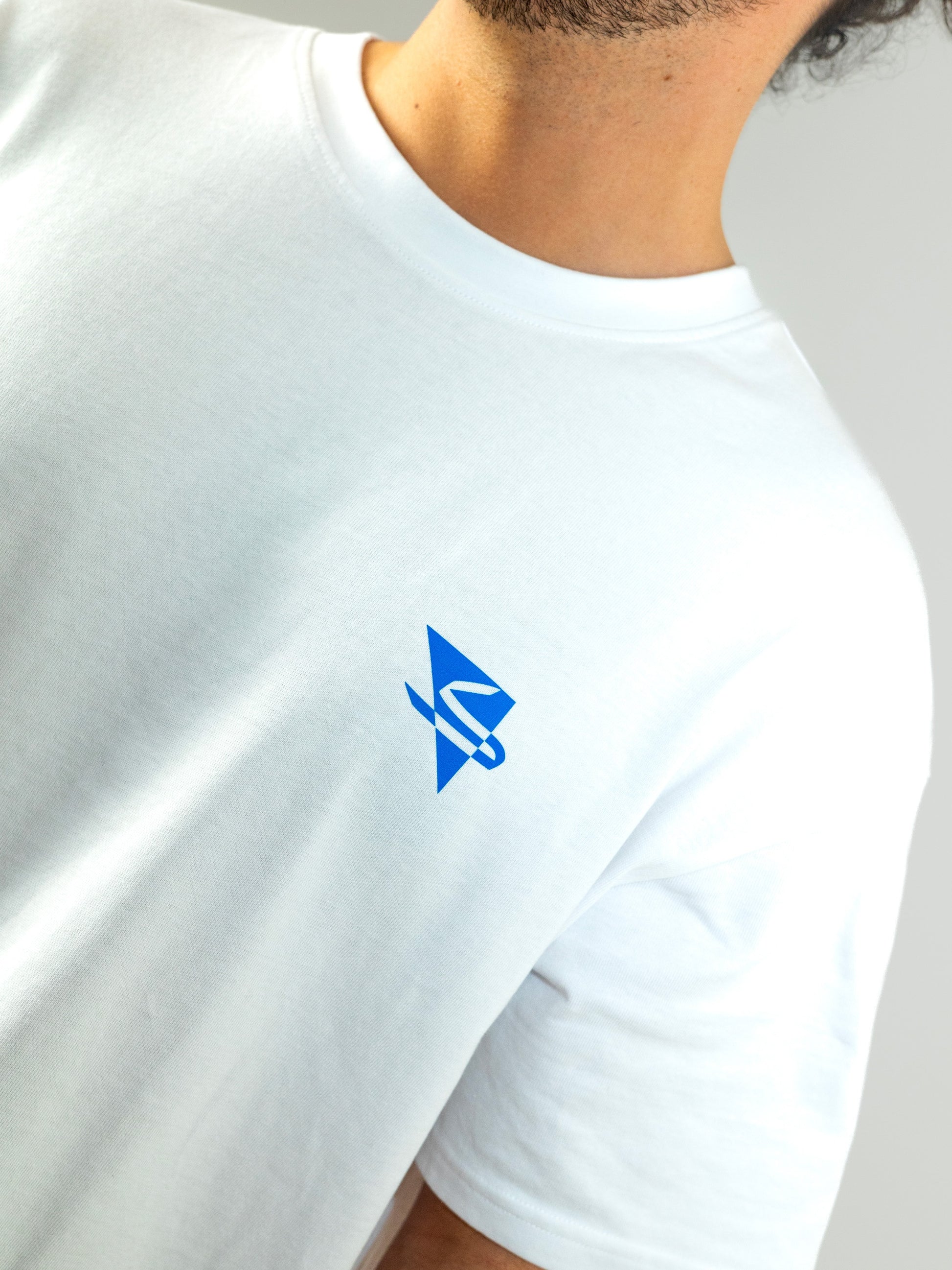 Close up of a beautiful arab model wearing a cool and creative over-sized t-shirt for streetwear and everyday lifestyle clothing. It features a simple beautiful logo, which is geometric in design and that has an arabic letter within it.  White t-shirt. Frontside view. Blue print color.