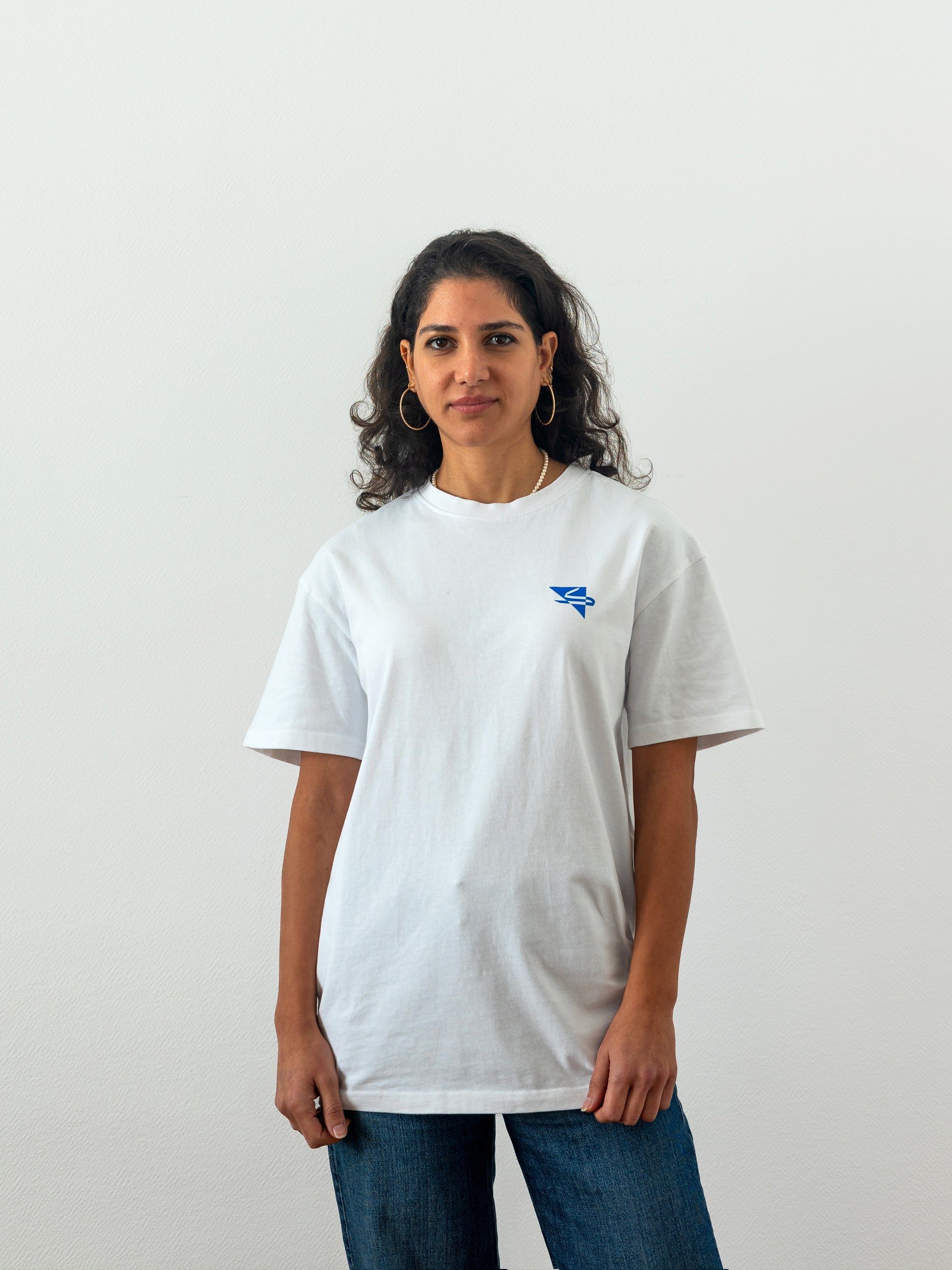 Beautiful arab female model wearing a cool and creative over-sized t-shirt for streetwear and everyday lifestyle clothing. It features a simple beautiful logo, which is geometric in design and that has an arabic letter within it.  White t-shirt. Frontside view. Blue print color.