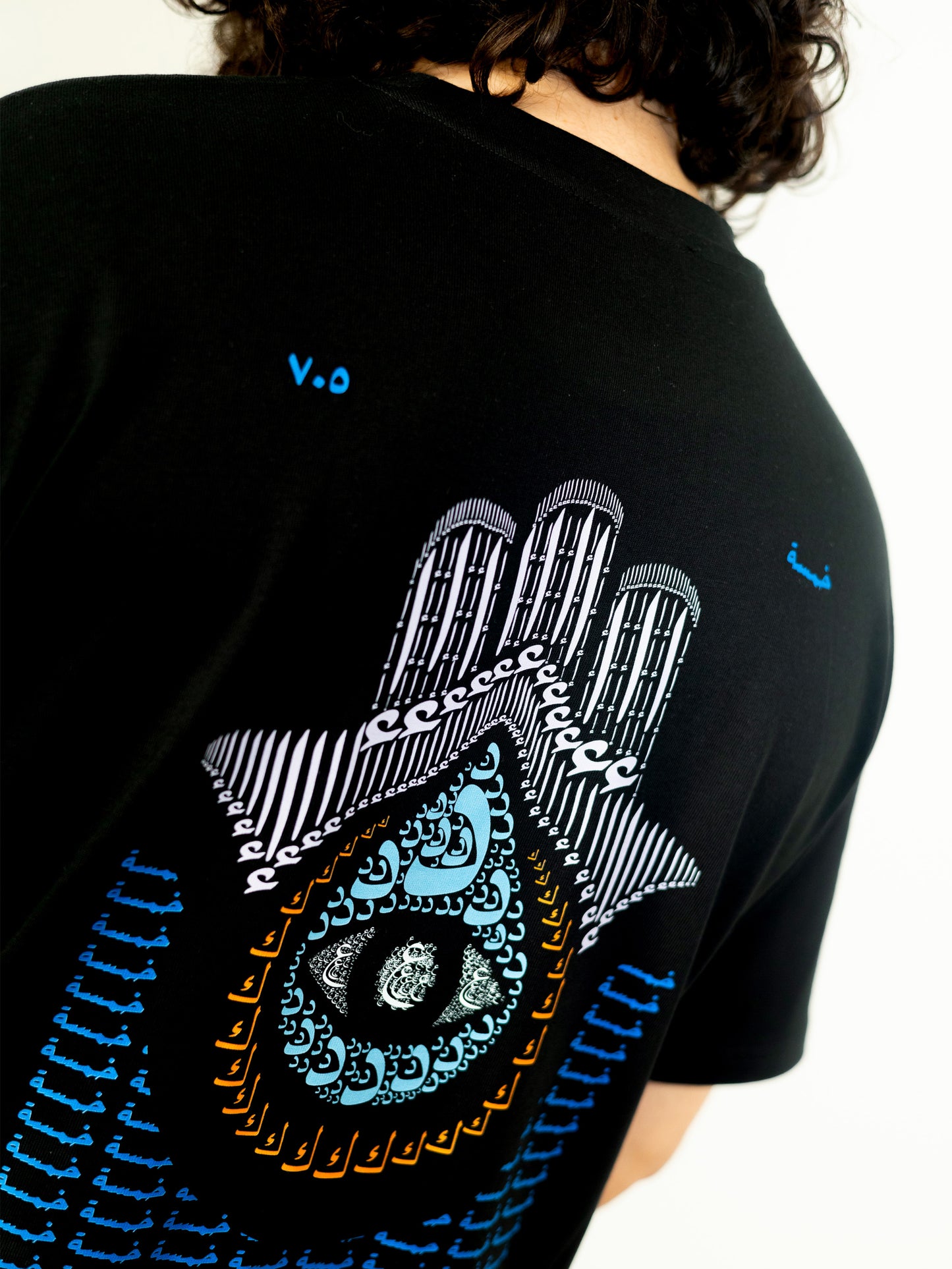 Close-up of a cool and creative over-sized t-shirt for streetwear and everyday lifestyle clothing. This product features an exclusive print about khamsa, also known as hamsa, or the hand of Fatima. It is a popular amulet in Middle Eastern and North African culture, and is intended to protect against evil and envy. This art piece and pattern uses beautiful arabic letters and calligraphy to form its attractive shape. Black t-shirt. Backside view. Black and blue print color.