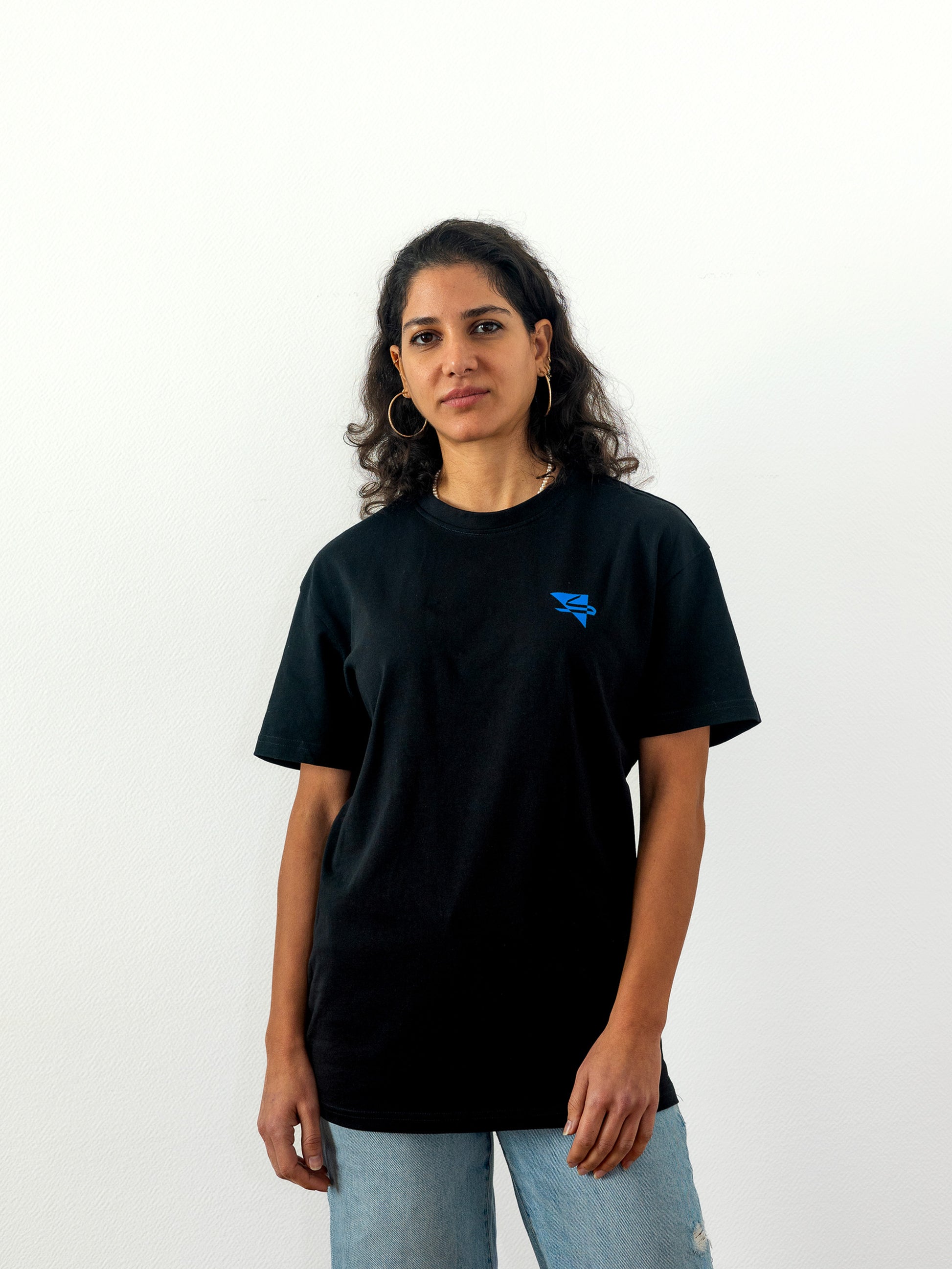 Beautiful female arab model wearing a cool and creative over-sized t-shirt for streetwear and everyday lifestyle clothing. It features a simple beautiful logo, which is geometric in design and that has an arabic letter within it. Black t-shirt. Frontside view. Black and blue print color.