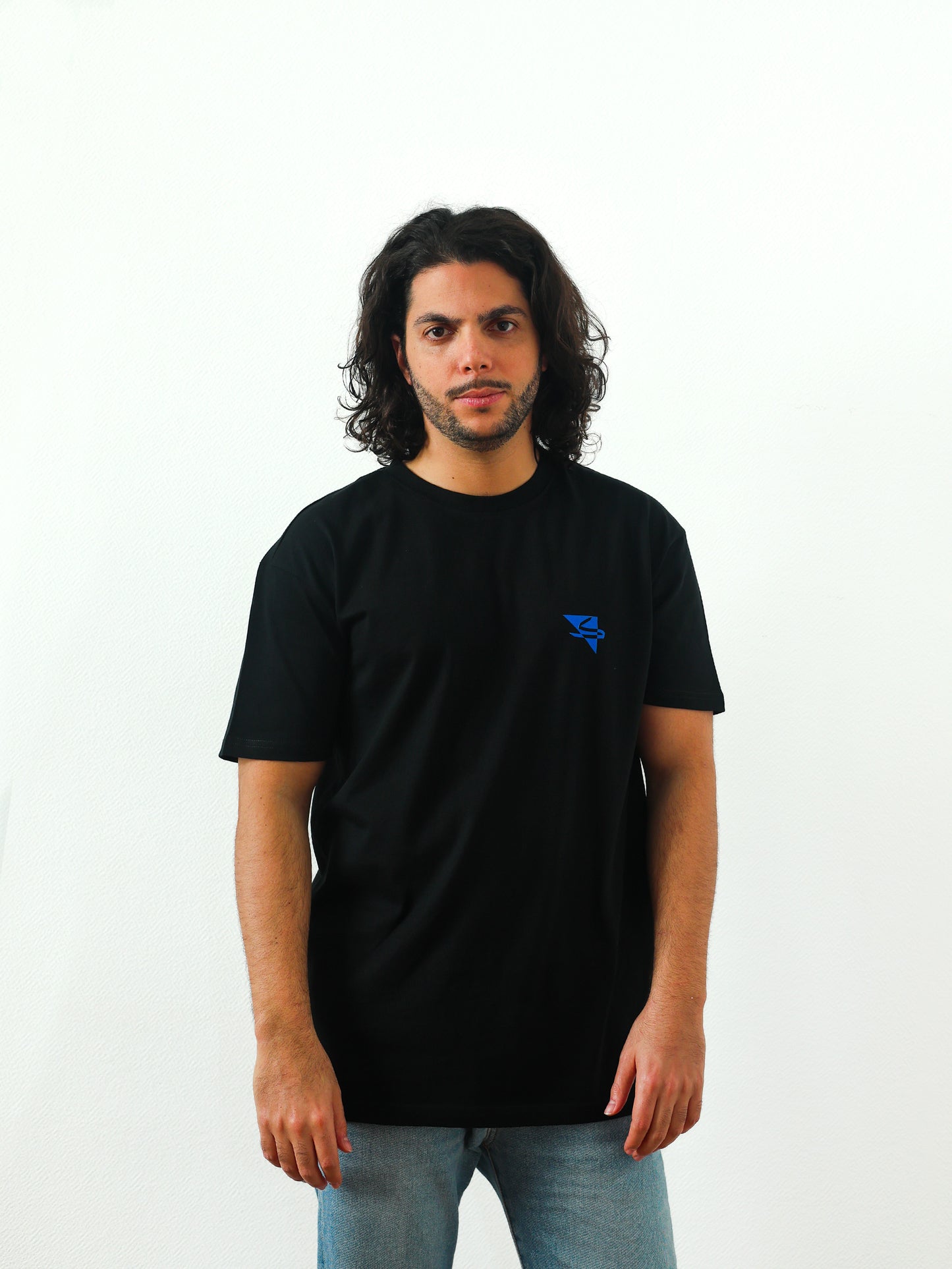 Beautiful male arab model wearing a cool and creative over-sized t-shirt for streetwear and everyday lifestyle clothing. It features a simple beautiful logo, which is geometric in design and that has an arabic letter within it. Black t-shirt. Frontside view. Black and blue print color.