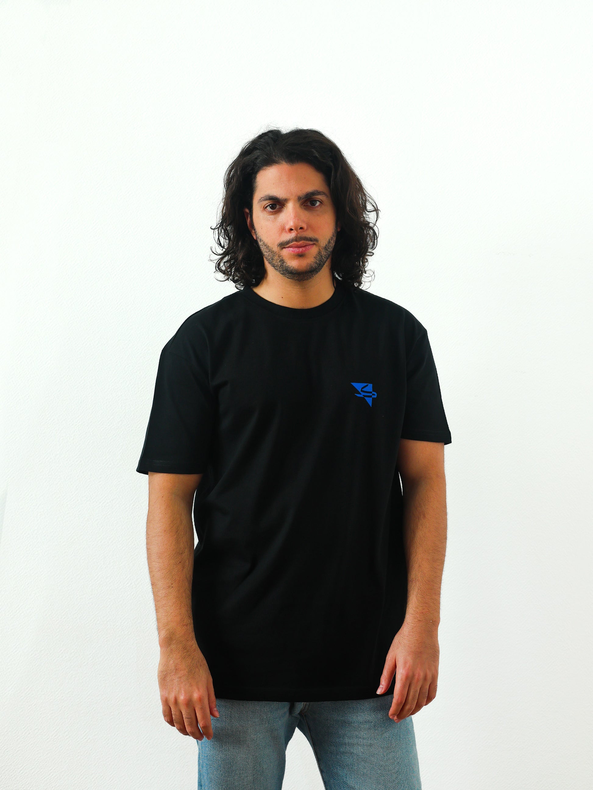 Beautiful male arab model wearing a cool and creative over-sized t-shirt for streetwear and everyday lifestyle clothing. It features a simple beautiful logo, which is geometric in design and that has an arabic letter within it. Black t-shirt. Frontside view. Black and blue print color.