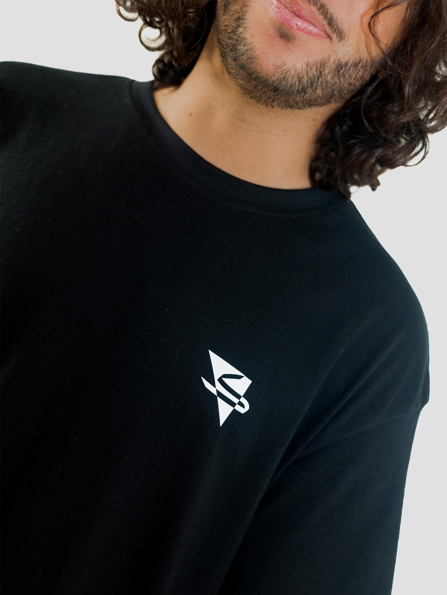 Close-up of a cool and creative over-sized t-shirt for streetwear and everyday lifestyle clothing. It features a simple beautiful logo, which is geometric in design and that has an arabic letter within it.  Black t-shirt. Frontside view. Black and white print color.