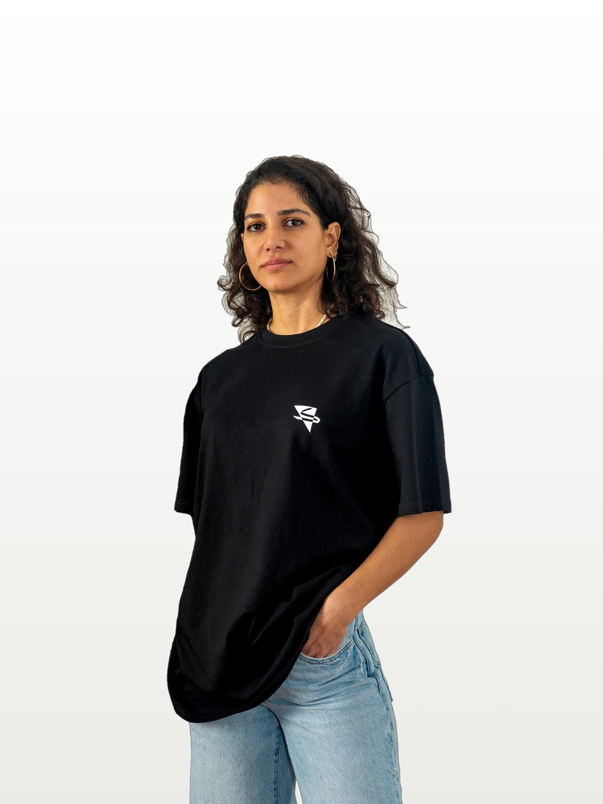 Beautiful, hot arab model wearing a cool and creative over-sized t-shirt for streetwear and everyday lifestyle clothing. It features a simple beautiful logo, which is geometric in design and that has an arabic letter within it.  Black t-shirt. Frontside view. Black and white print color.
