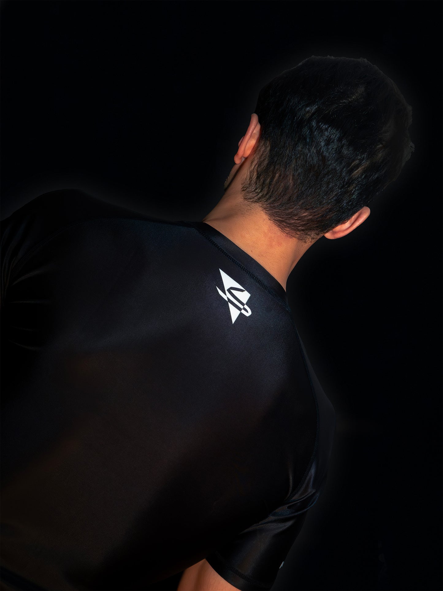 Black rashguard with arabic logo used for training jiu-jitsu and other martial arts (e.g. MMA). Back view. Black and white print color. Close-up.