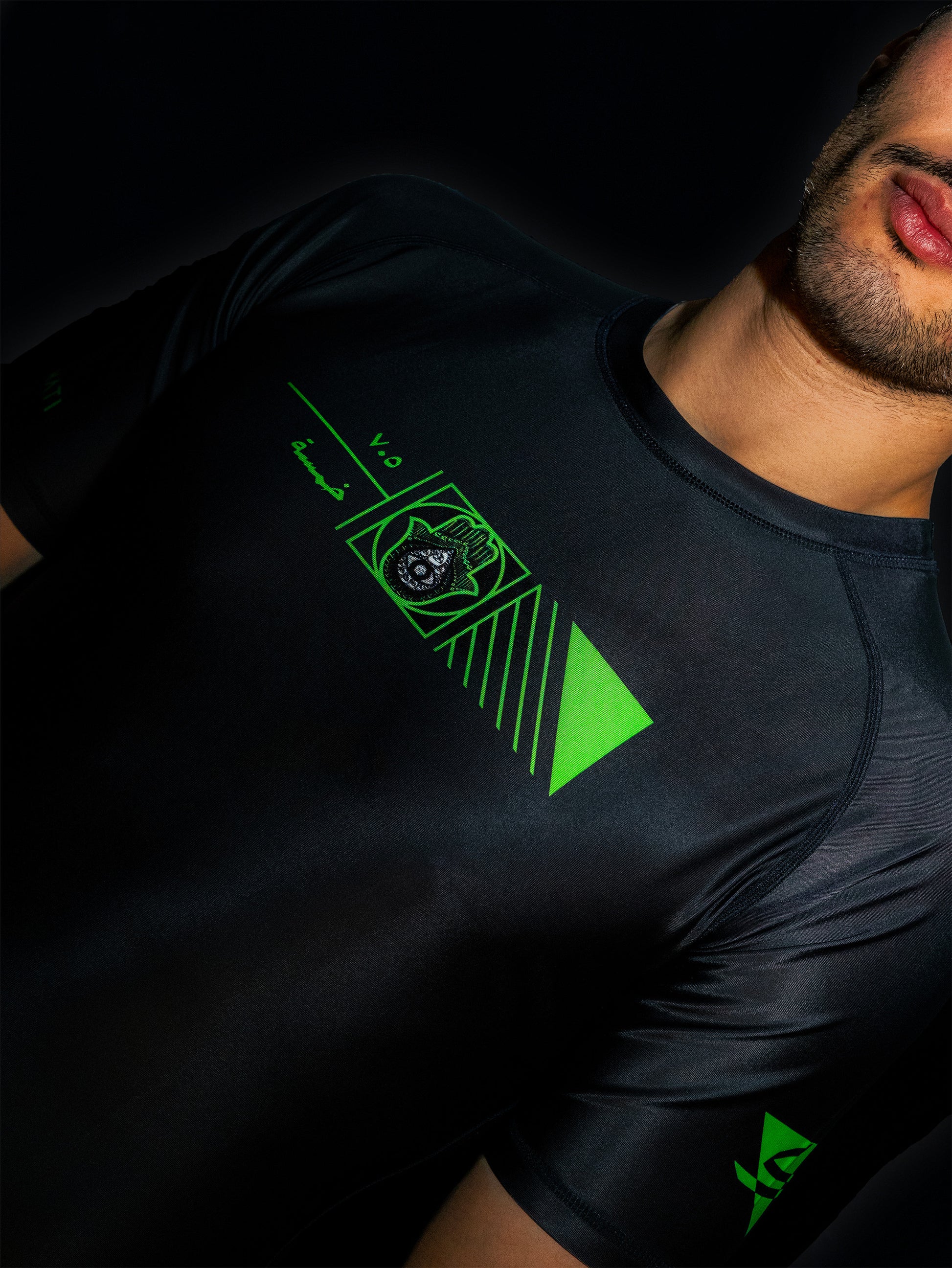 Black rashguard with arabic design, used for jiu-jitsu and other martial arts (e.g. MMA). This product features an exclusive print about khamsa, also known as hamsa, or the hand of Fatima. It is a popular amulet in Middle Eastern and North African culture, and is intended to protect against evil and envy. This art piece and pattern uses beautiful arabic letters and calligraphy to form its attractive shape. Yellow and white print color. Arab model wearing it. Front-side close-up