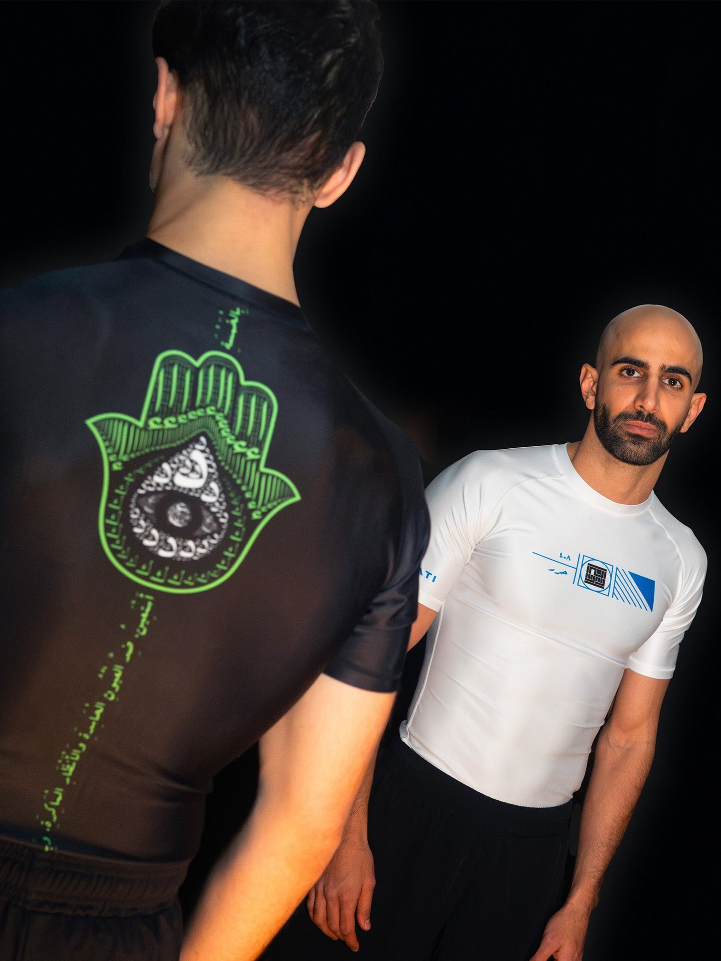Two arabic fighters and martial artists facing each other. Each is wearing a cool, unique ashguard for jiujitsu and other combat sports. One is wearing white and blue, and the other black and green , with a khamsa symbol.