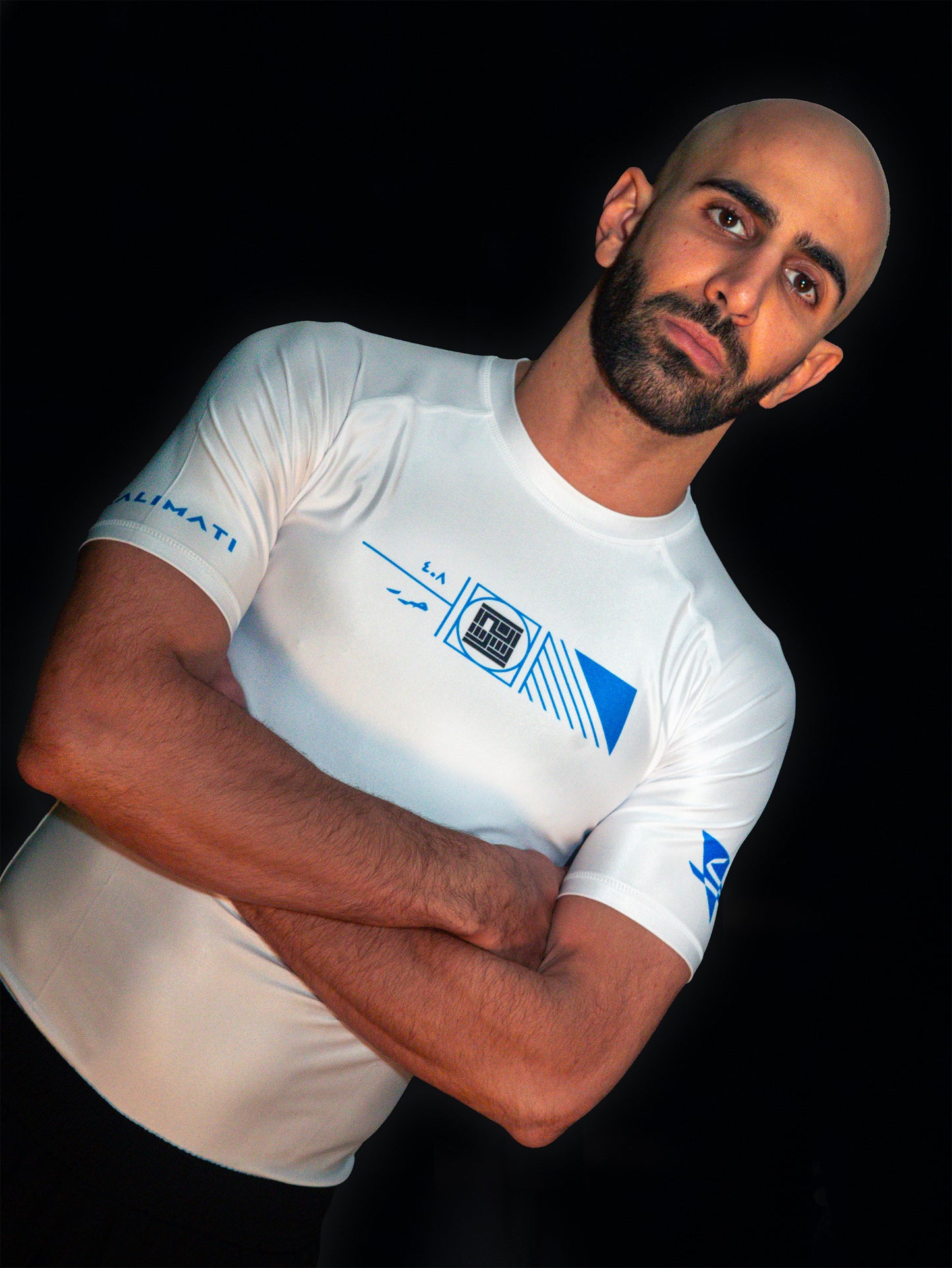 Arabic fighter wearing white rashguard with arabic print, used for jiu-jitsu and other martial arts (e.g. MMA). This product features an exclusive print emphasizing liberation of the individual and of society. Inspired by different types of arabic calligraphy, namely Kufic script, it exhibits a series of beautiful, geometrical circles and shapes. It is also draws from Japanese art and tribal design, highlighting the importance of spiritual freedom. Front view and closeup. Blue and black print color.